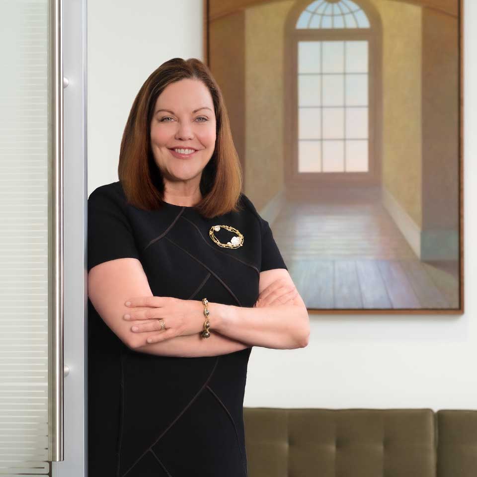 Cheryl Holland standing with arms crossed in front of a painting of a window hung over a couch.