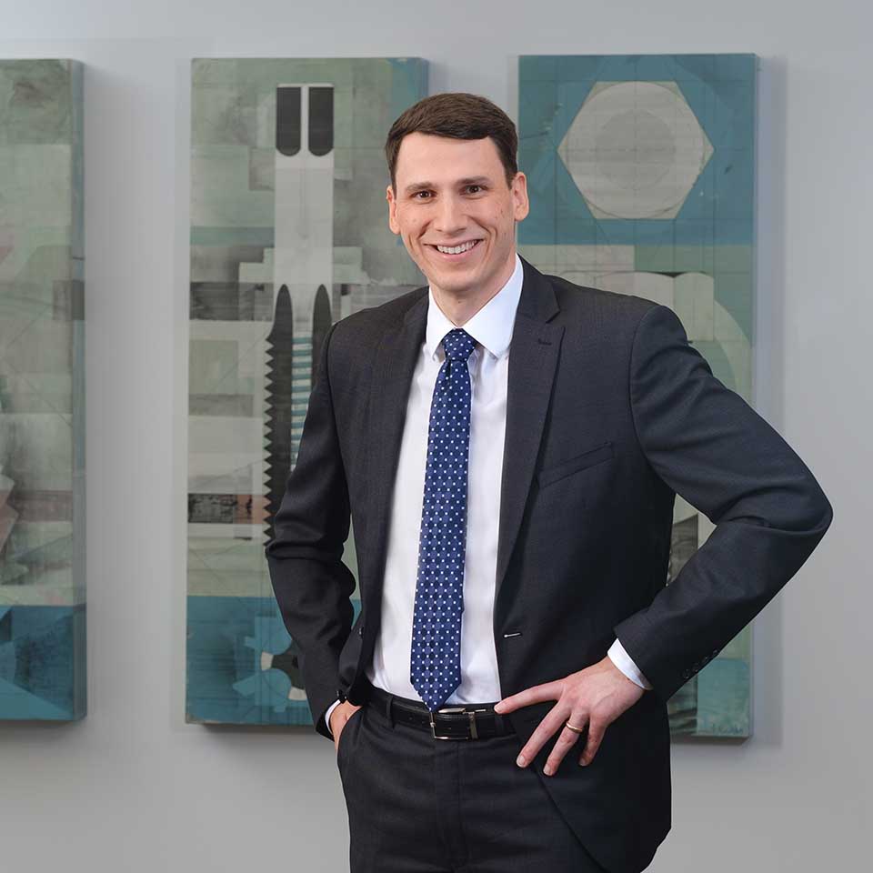 Stephen Maggard standing with hands on hips in front of a triptych of abstract paintings.