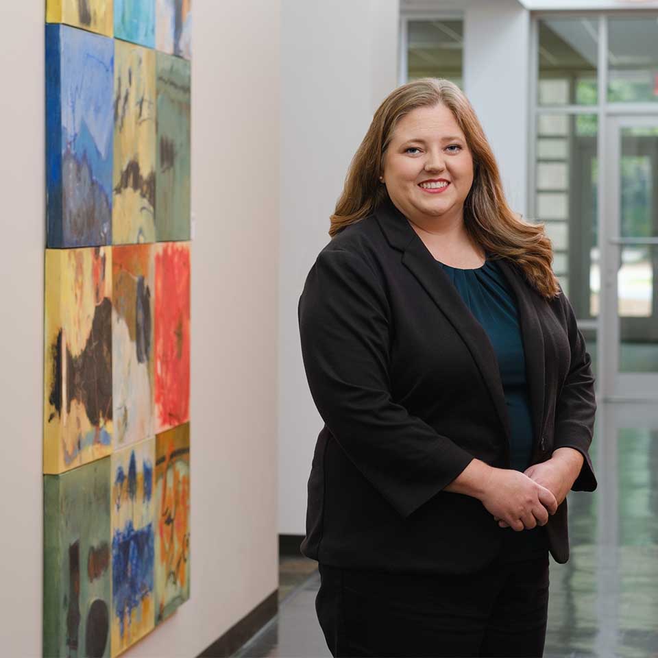 Abigail Mason standing in front of a grid of abstract paintings.