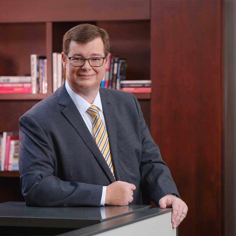 Scotty Scott seated at a desk in front of a polished wood bookcase.