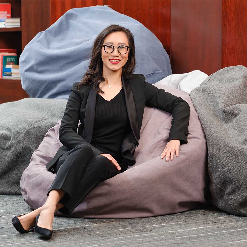 Kathy Guo seated on a pile of bean bag chairs in a black tailored suit and heels.