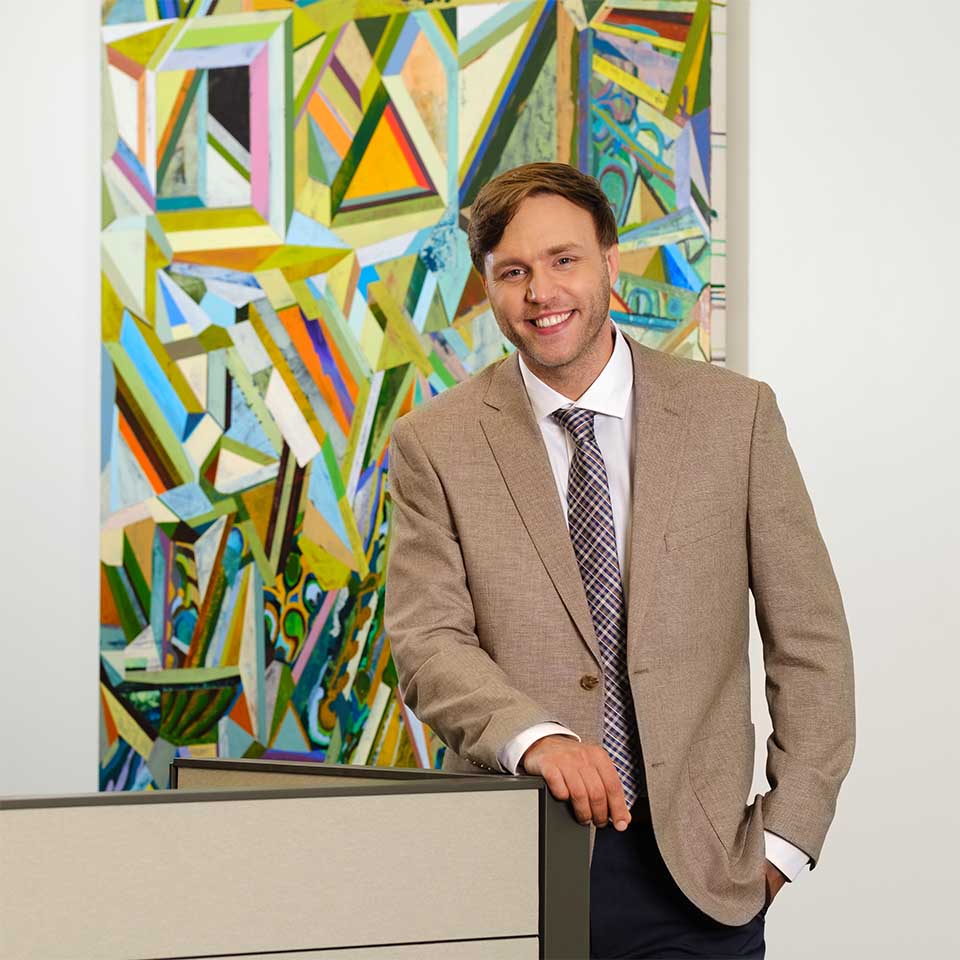 Michael Holland standing in front of a large, colorful abstract mural of geometric shapes.